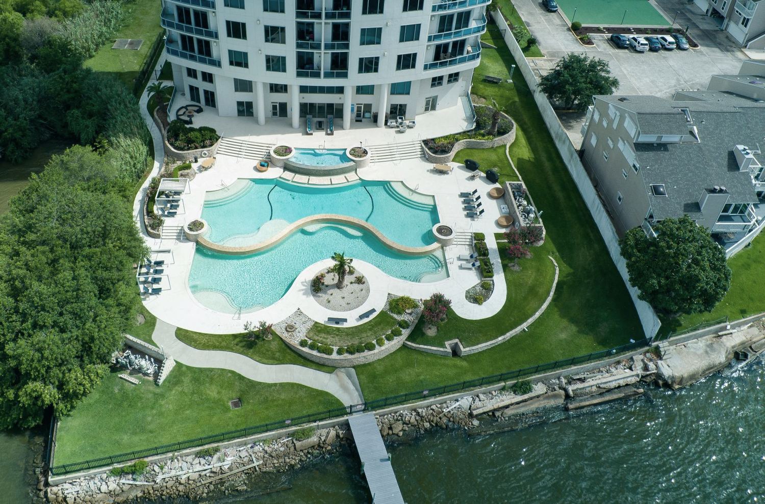 Aerial view of a waterfront condominium amenity deck in the Houston area, with a main pool, a separate spa and a lower freeform pool.